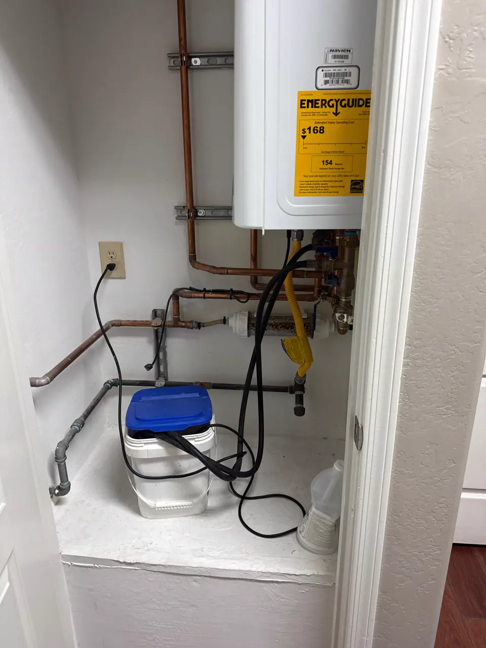 A tankless water heater connected to a bucket and service hoses for flushing