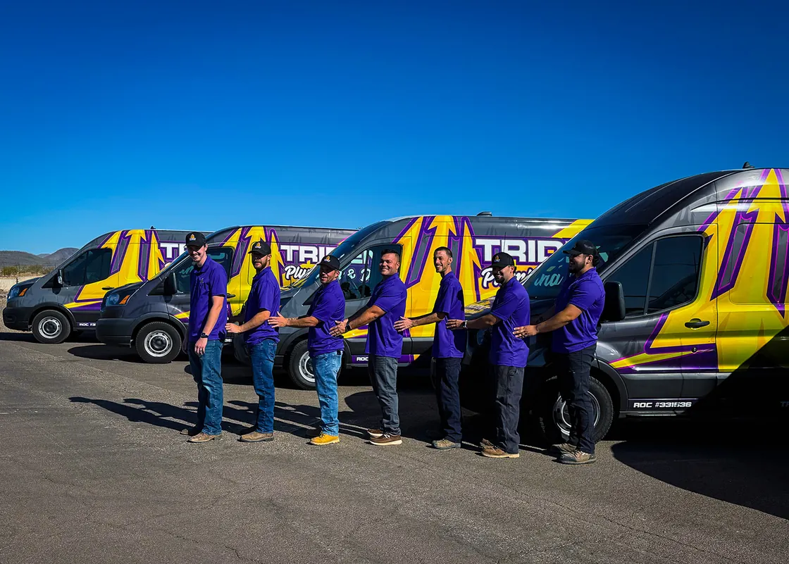 Six Trident team members in purple shirts standing in a line beside their service vans