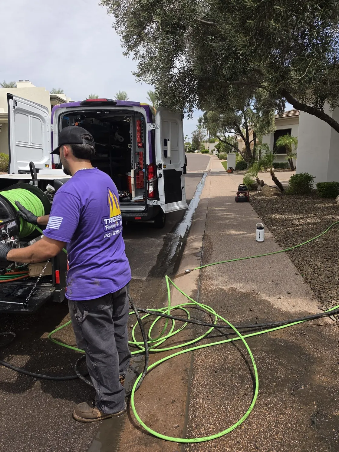 A Trident technician at a trailer-mounted jetter with green hose laid toward the house