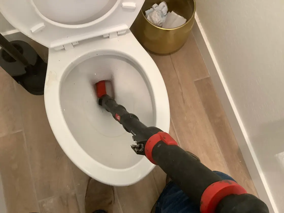 A technician using a toilet auger at a clogged toilet