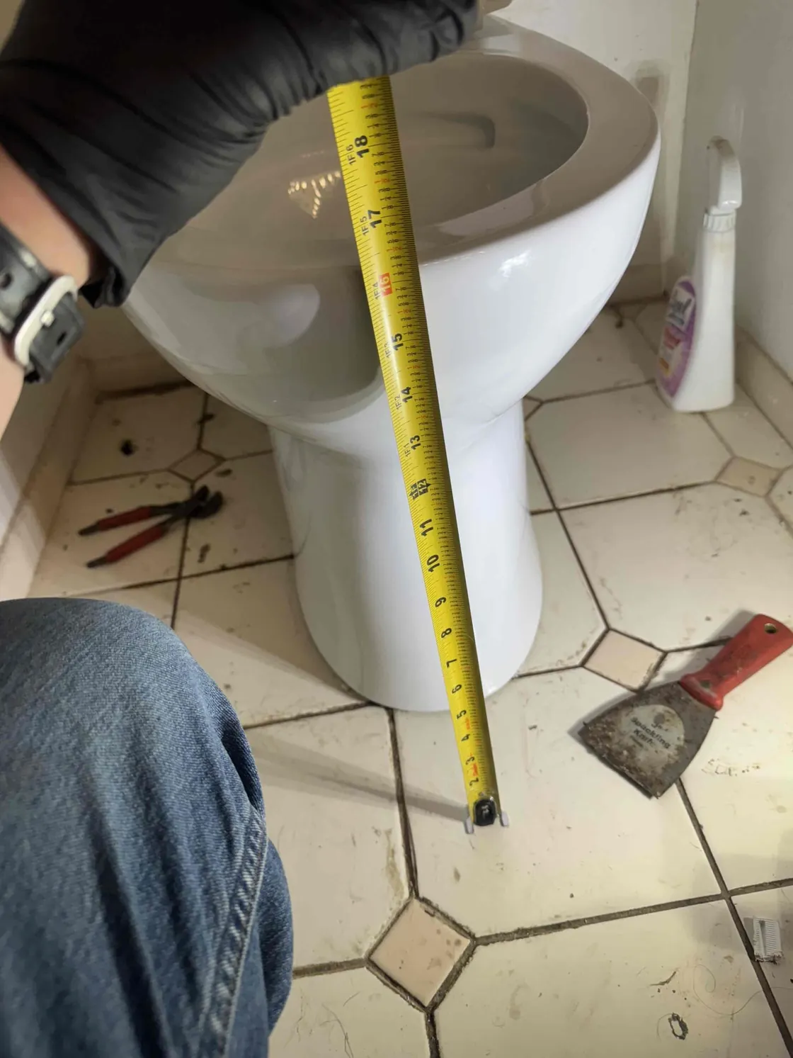 A gloved hand holding a tape measure beside a toilet
