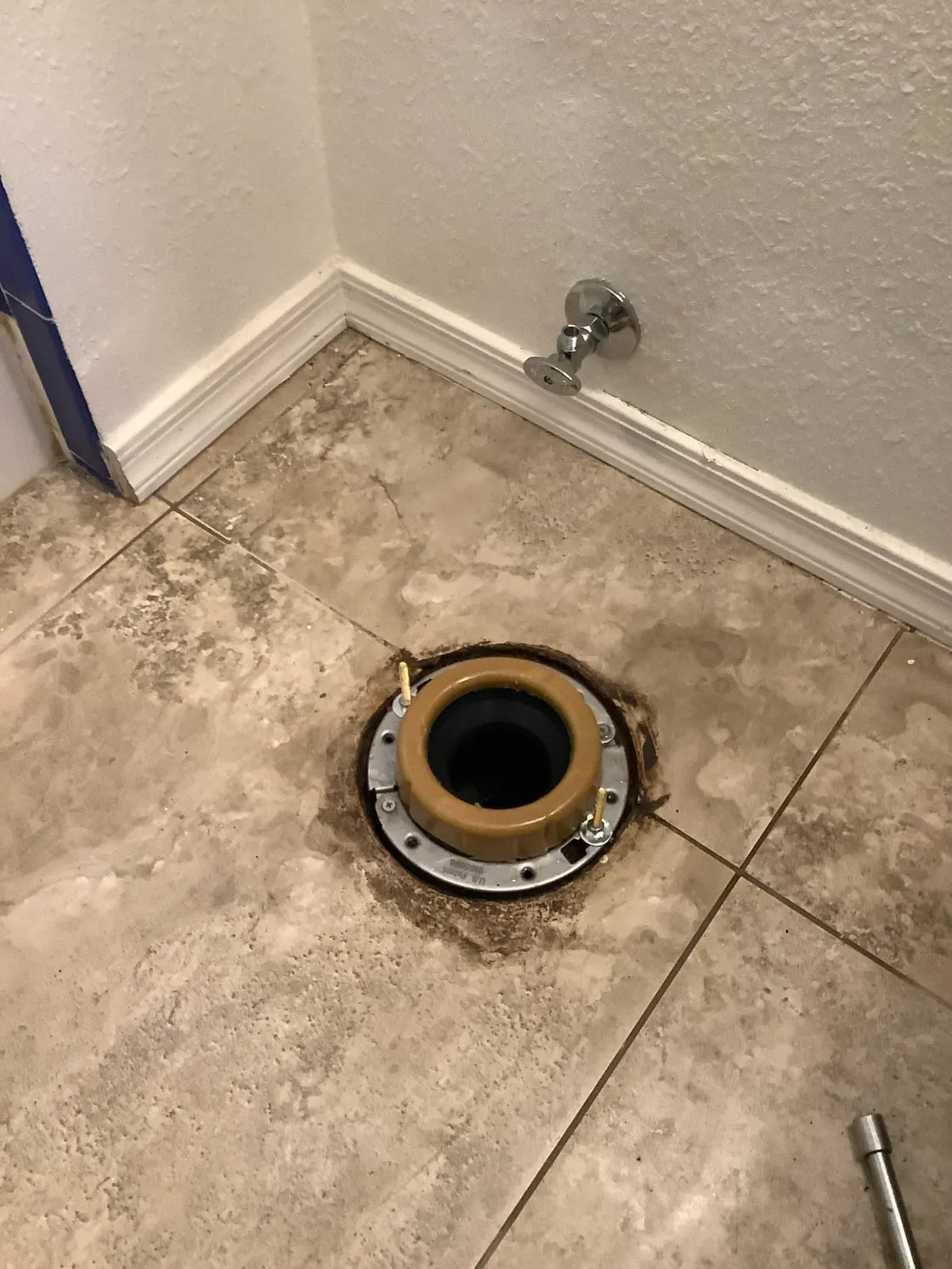 A toilet flange and wax ring exposed on a tiled bathroom floor