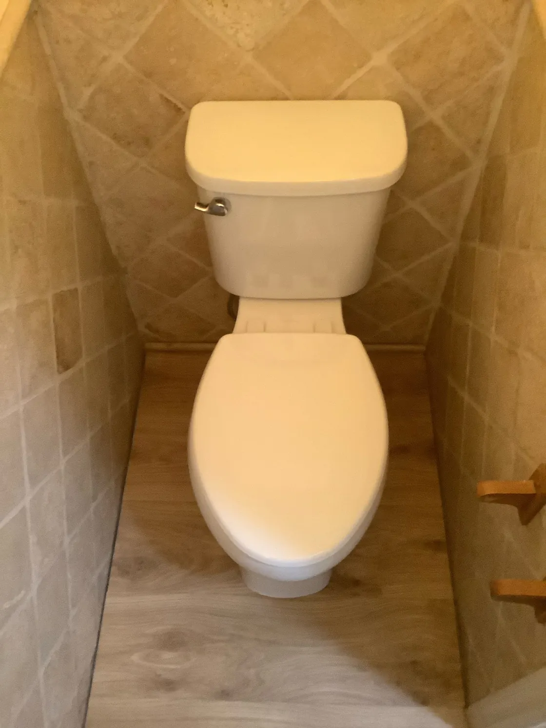 A white toilet in a narrow alcove with tan tile walls