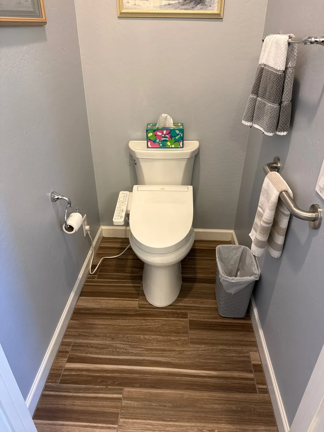 A white toilet with a bidet seat in a small bathroom with wood-look flooring