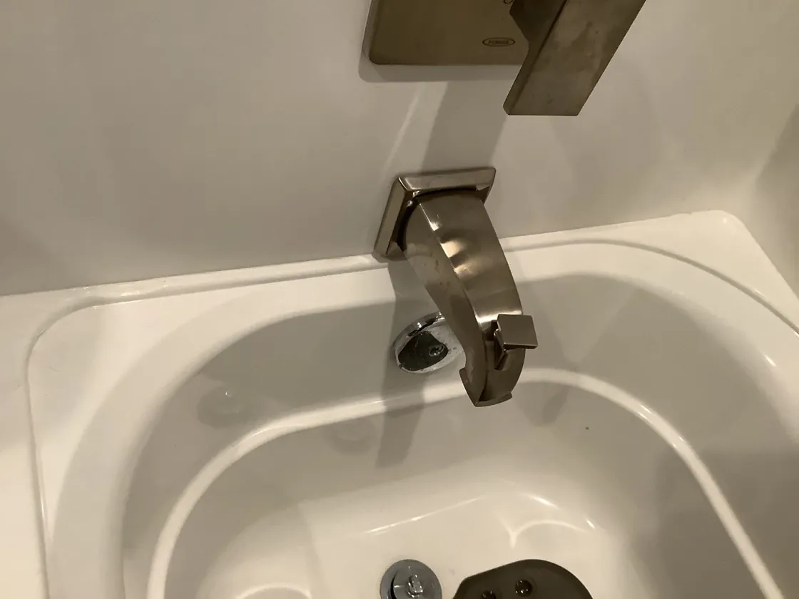 A brushed nickel tub spout over a white bathtub drain