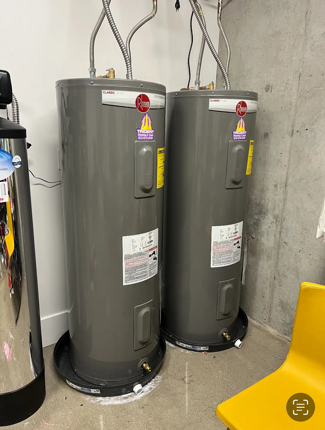 Two electric tank water heaters installed side by side on drain pans
