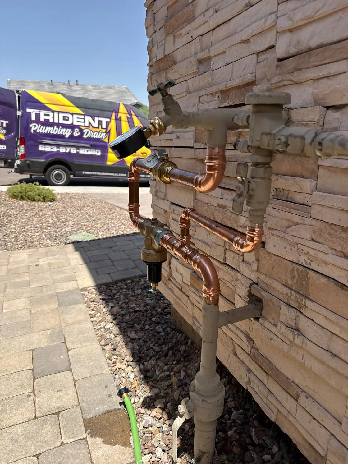 Copper water supply piping on a stacked-stone wall with a Trident van parked in the background