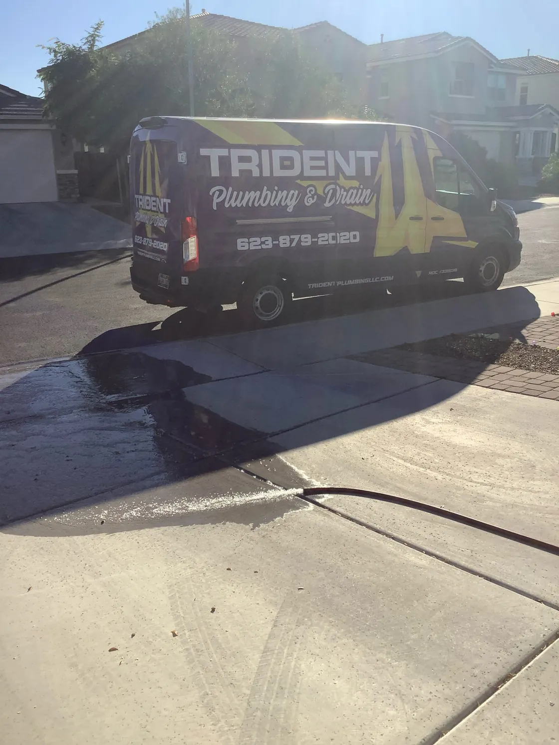 A Trident van at the curb with a service hose running across a wet driveway