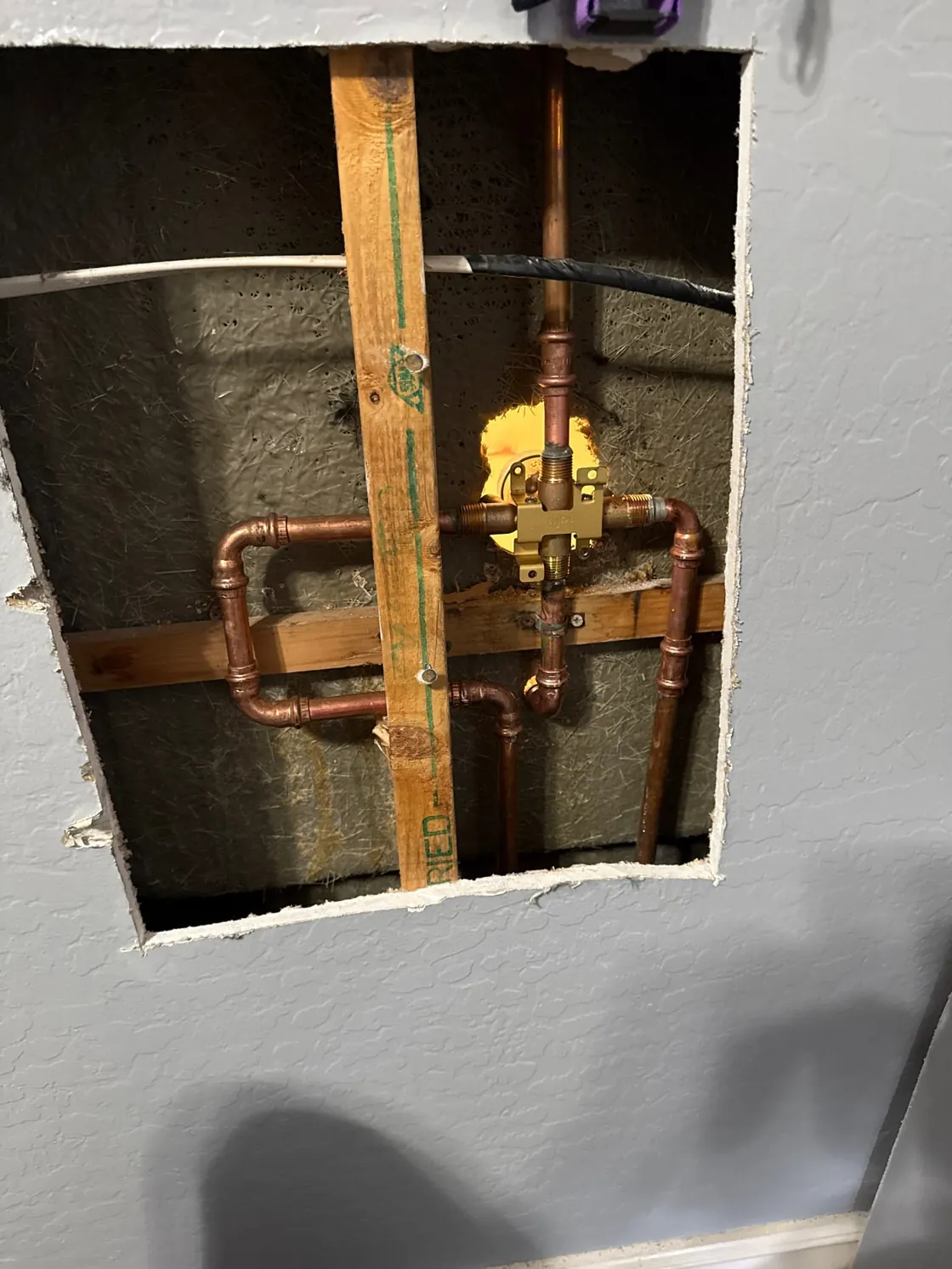 Copper water lines and a valve visible through an opening cut in a wall