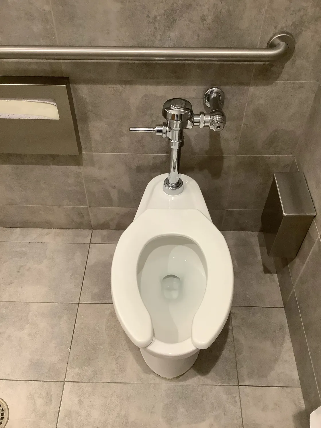 A wall-mounted urinal and flush valve in a commercial restroom