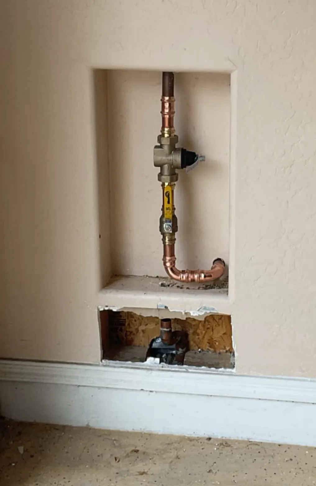 Copper piping and a regulator in a wall niche, with an access opening cut below