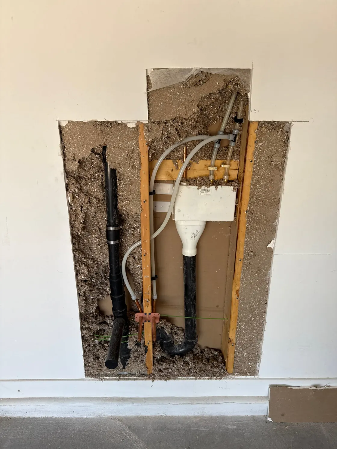 An opened wall exposing supply and drain piping in the wall cavity