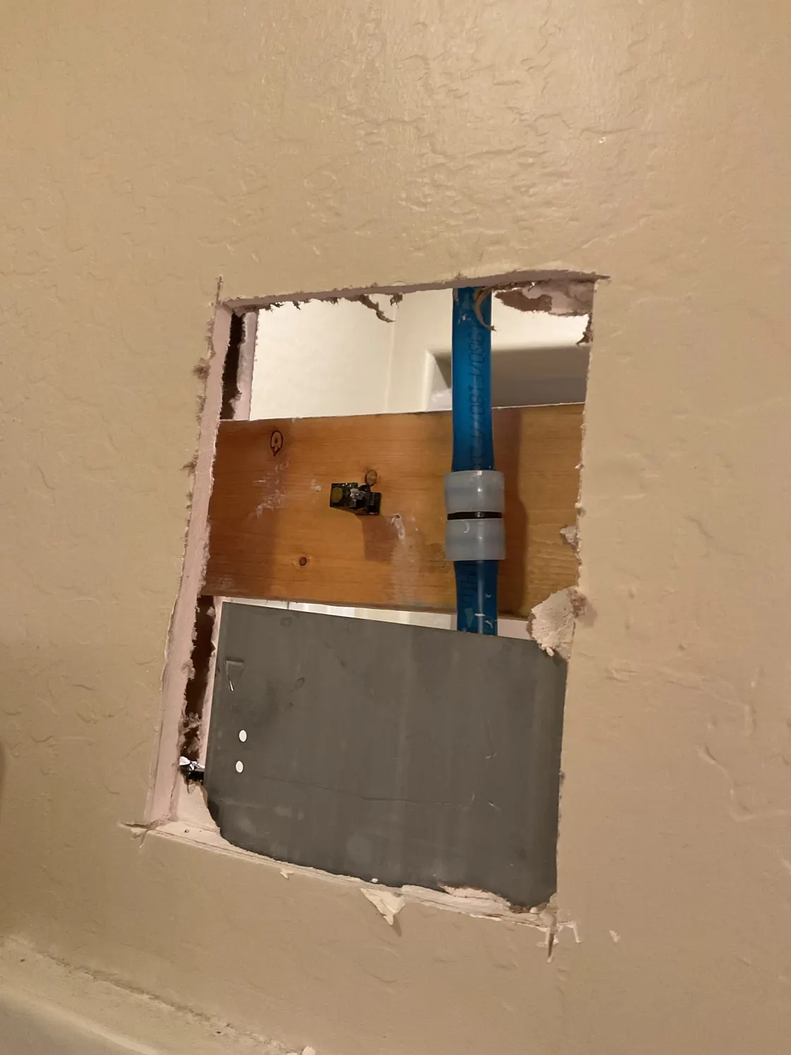 An opening in a wall exposing blue water-supply piping for a repair