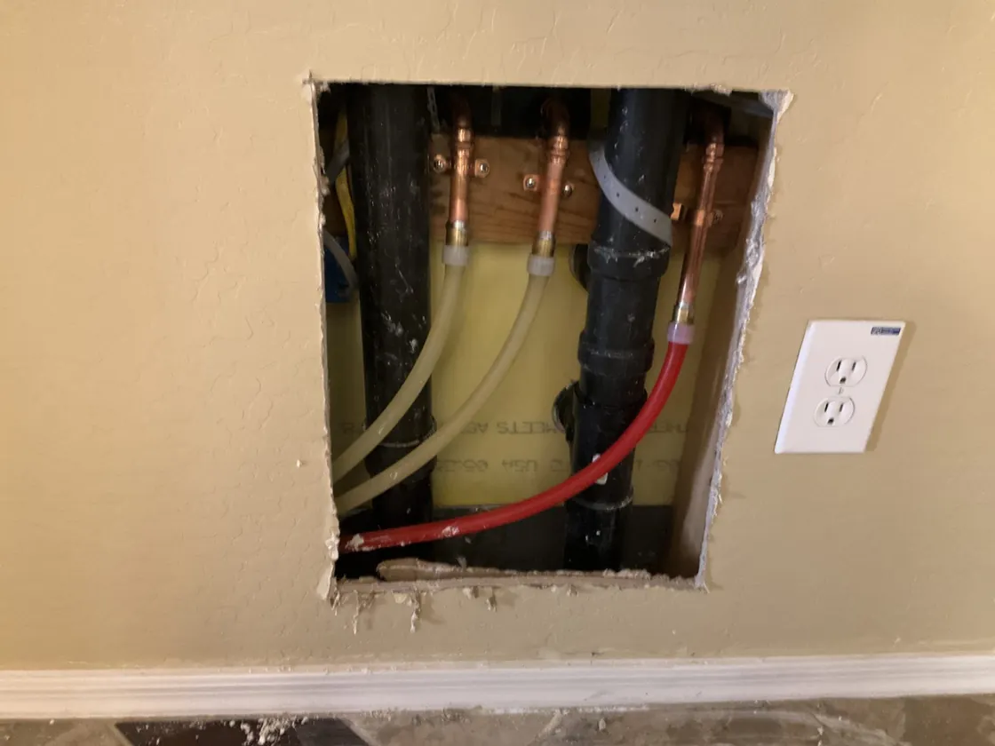 Red and blue water-supply lines exposed through a wall opening