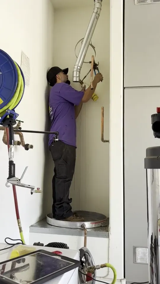 A Trident technician working on pipe connections above a tank water heater