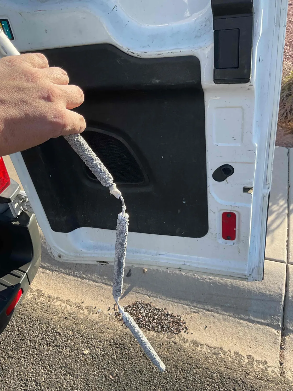 A person holding a worn water heater anode rod beside a service van