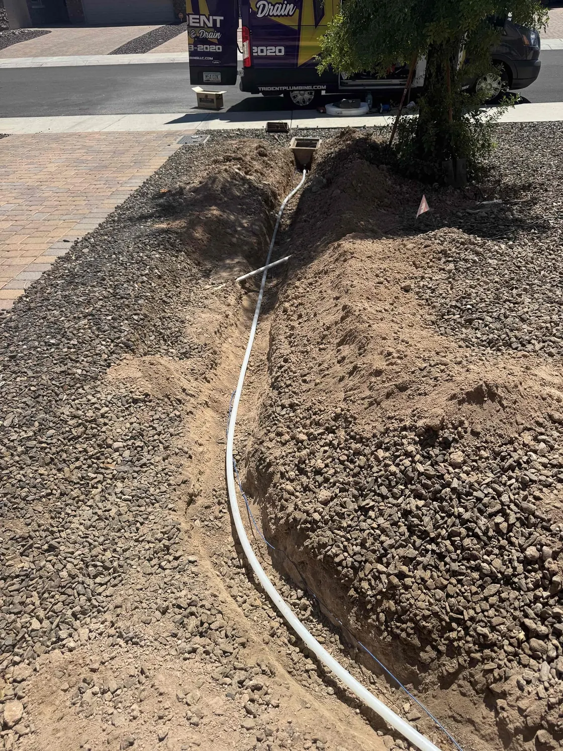 A narrow trench through a gravel yard with a white water line laid along it