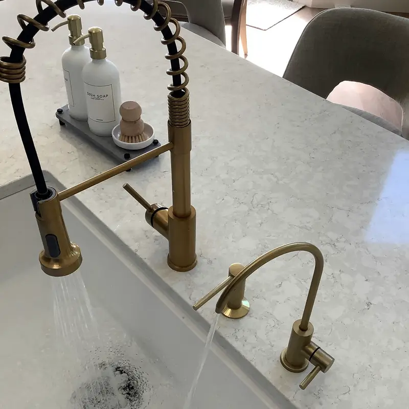 Gold kitchen faucet and smaller drinking-water faucet at a finished sink