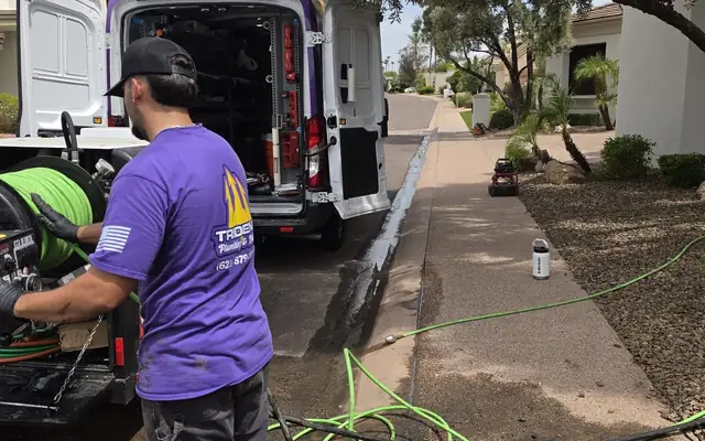 Trident technician running a hydro jetting hose from the service van