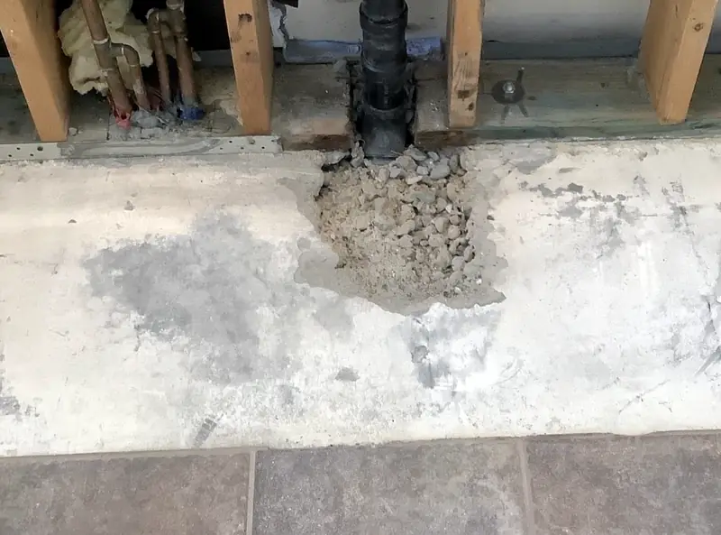 A drain line where the concrete slab has been broken out around it for a slab leak repair, with the wall opened above