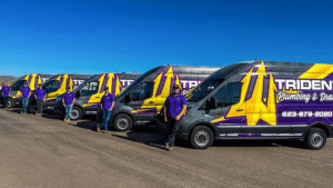 A line of Trident Plumbing service vans parked side-by-side with team members standing in front of them in Phoenix.