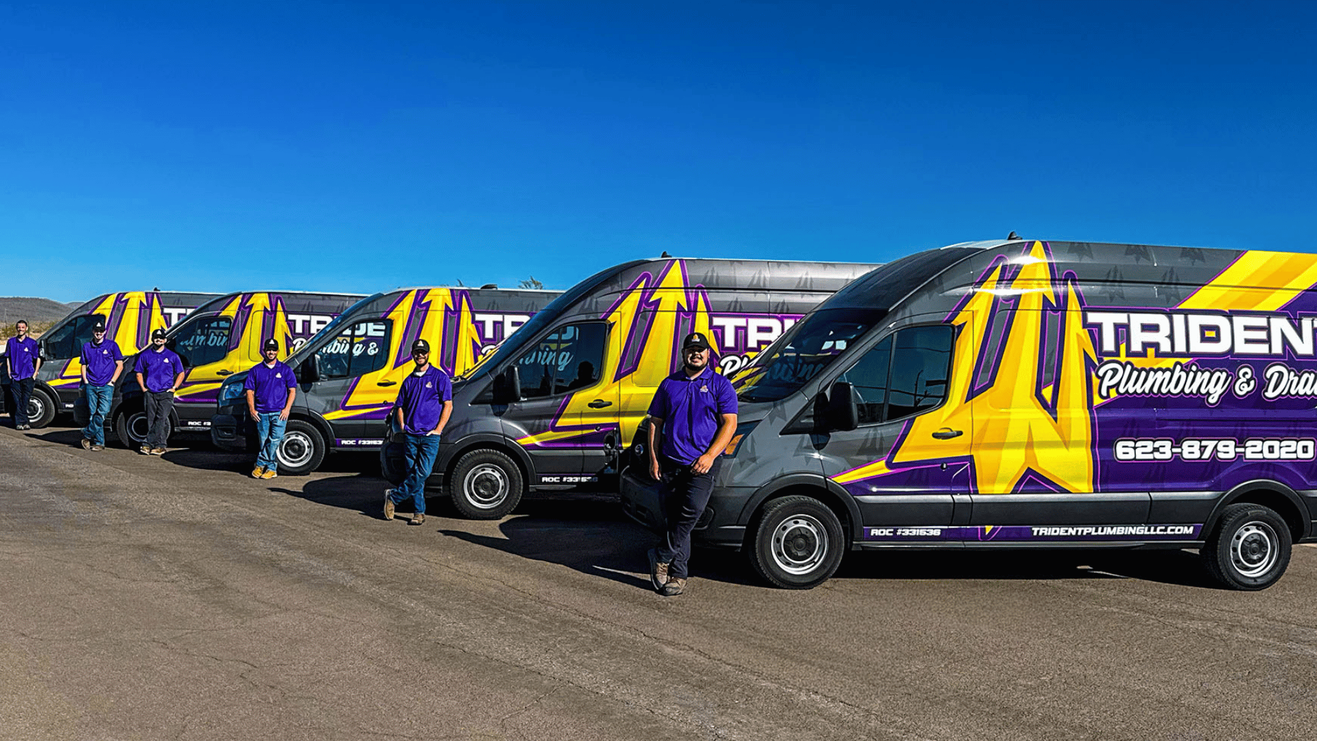 A line of Trident Plumbing service vans parked side-by-side with team members standing in front of them in Phoenix.