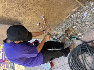 A plumber using a professional pressure gauge to check the water pressure at an outdoor residential hose bibb.
