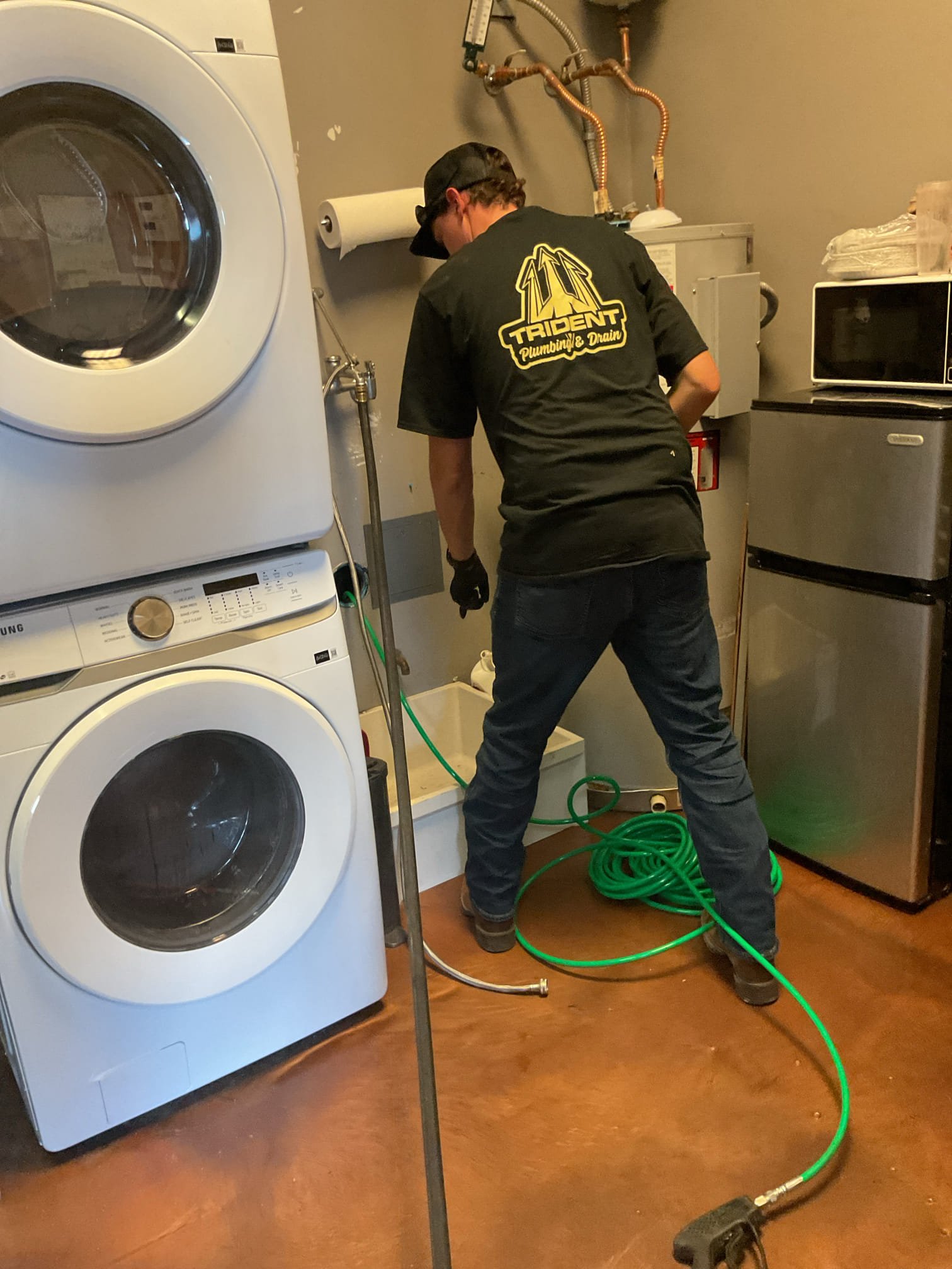 Trident Plumbing technician performing professional tankless water heater maintenance in a residential laundry room.