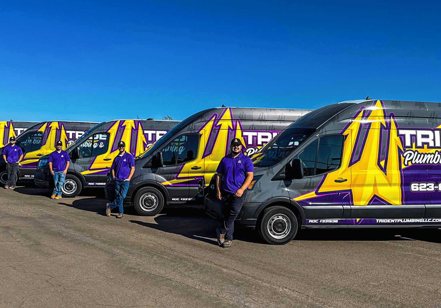 A line of Trident Plumbing service vans parked side-by-side with team members standing in front of them in Phoenix.