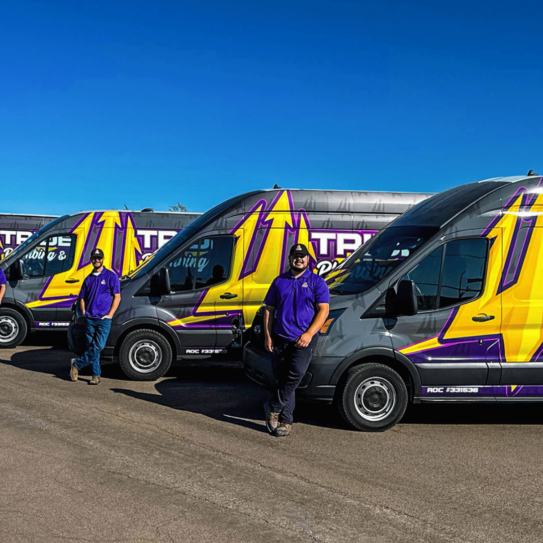 A line of Trident Plumbing service vans parked side-by-side with team members standing in front of them in Phoenix.